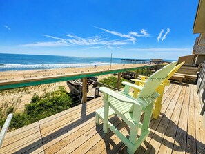 A wooden deck with chairs overlooking a beach and ocean.
