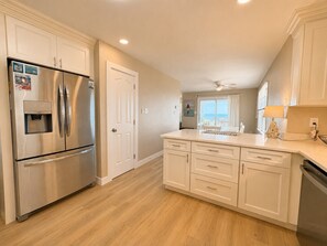 Una cocina con refrigerador de acero inoxidable, gabinetes blancos, dispensador de agua y ventilador de techo.