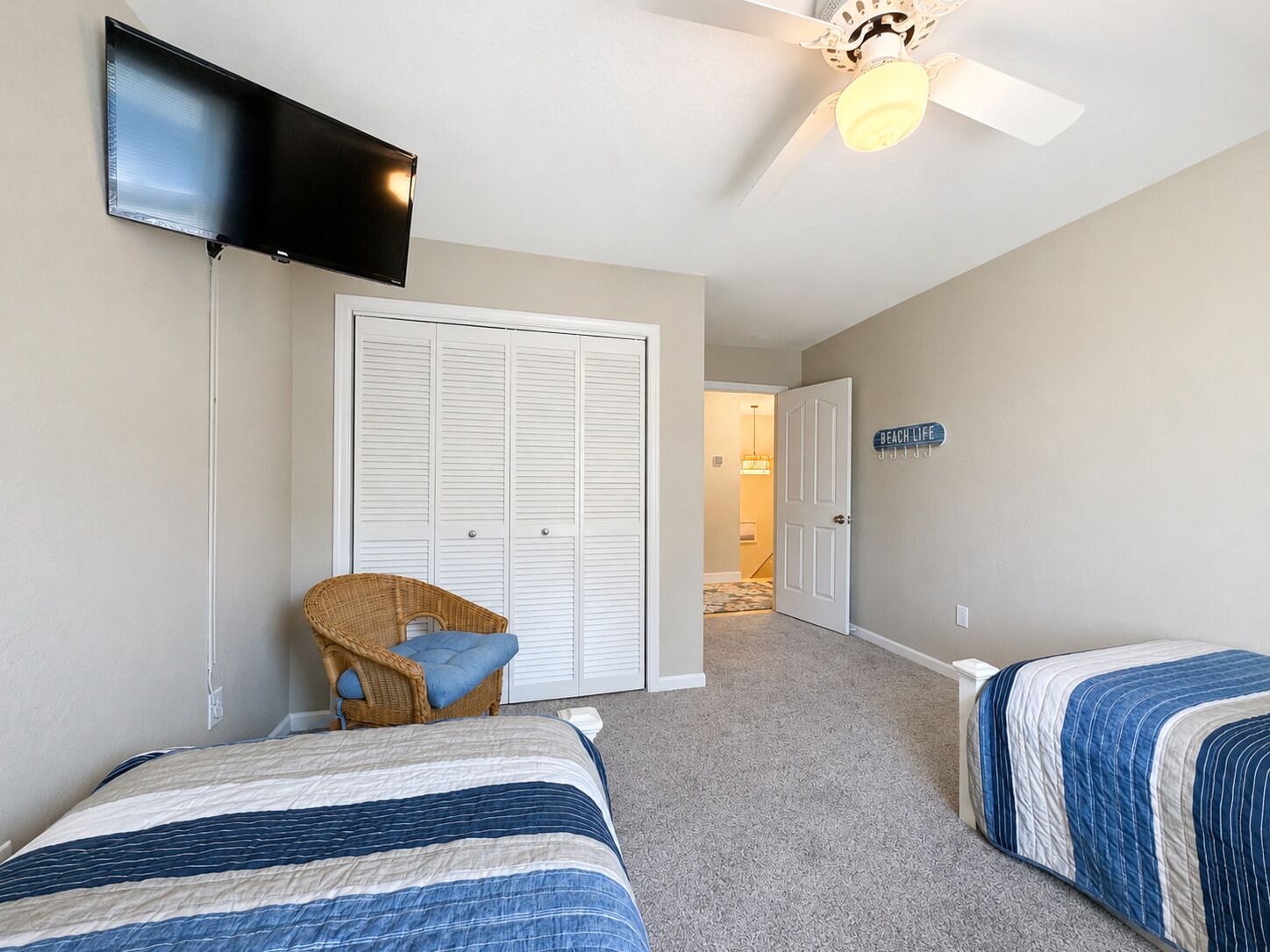 A bedroom with two beds, a television, a ceiling fan, and a wardrobe.