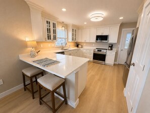 A kitchen with white cabinetry, a central island with stools, a microwave, a stove, and a refrigerator.