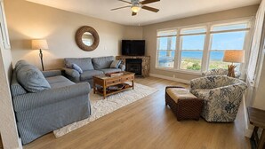 A living room with a sofa, armchair, coffee table, fireplace, TV, and large windows with a view. - A Sense of Porpoise - 4 BR Oceafront Townhome in Southern Shores (Southern Shores)