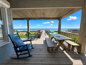 A wooden deck with a rocking chair and picnic table, overlooking a beach with a clear sky. - A Sense of Porpoise - 4 BR Oceafront Townhome in Southern Shores (Southern Shores)