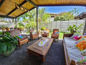 Un patio al aire libre con muebles de madera, una mesa con un mantel de encaje y varias plantas en macetas.