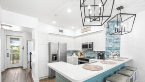 Cocina moderna con armarios blancos, una isla verde azulada y taburetes de bar.