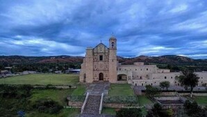 Un edificio grande y histórico con una torre central y una fachada simétrica, rodeado por un césped cuidado y senderos.