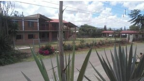 Un edificio de dos pisos con techo rojo, rodeado de vegetación y un cielo despejado.