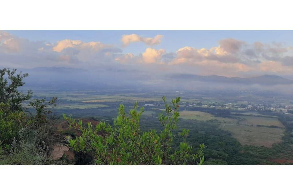 Vista panorámica de un paisaje con montañas a lo lejos, cielo despejado y algo de vegetación en primer plano.