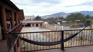 Un balcón con una hamaca, vista a un patio interior y montañas a lo lejos.