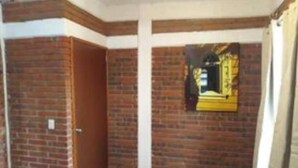 A room with brick walls, a wooden door, and a yellow-framed mirror on the wall. - Single Apartment Ara (Santo Domingo Yanhuitlán)