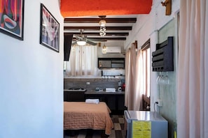 A compact hotel room with a kitchenette, a bed with a beige blanket, a ceiling fan, and a mounted TV. - Isla Mujeres Studio: Sea Views, AC & Kitchen (Isla Mujeres)