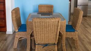 Un ensemble de salle à manger en osier, comprenant une table en verre et des chaises rembourrées de coussins bleus.