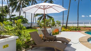 Une terrasse avec des fauteuils de jardin en osier, un parasol blanc et une piscine.