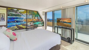 Un cuarto de hotel con una cama grande, un cuadro de un paisaje tropical, un televisor y un balcón con vista al océano.