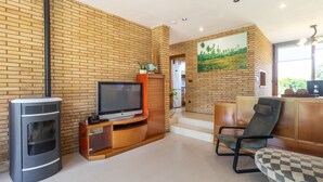 Una sala de estar con televisión sobre un mueble de madera, chimenea, sofá y un reposapiés a cuadros.