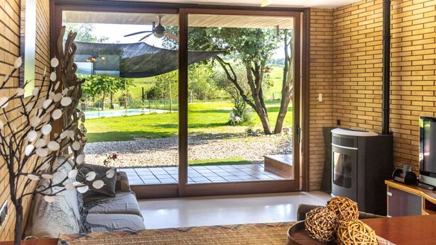 Una habitación acogedora con un amplio ventanal corredizo que da a un jardín, un ventilador de techo, una chimenea y un televisor.