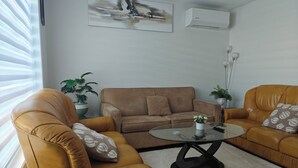 Una sala de estar con un sofá de cuero marrón, una mesa de centro de vidrio y dos plantas en macetas.