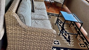 Ein Balkon mit einem Rattan-Sofa, zwei Stühlen, einem kleinen Tisch und einem gemusterten Teppich.