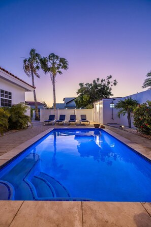 A swimming pool with lounge chairs, palm trees, and a white building.