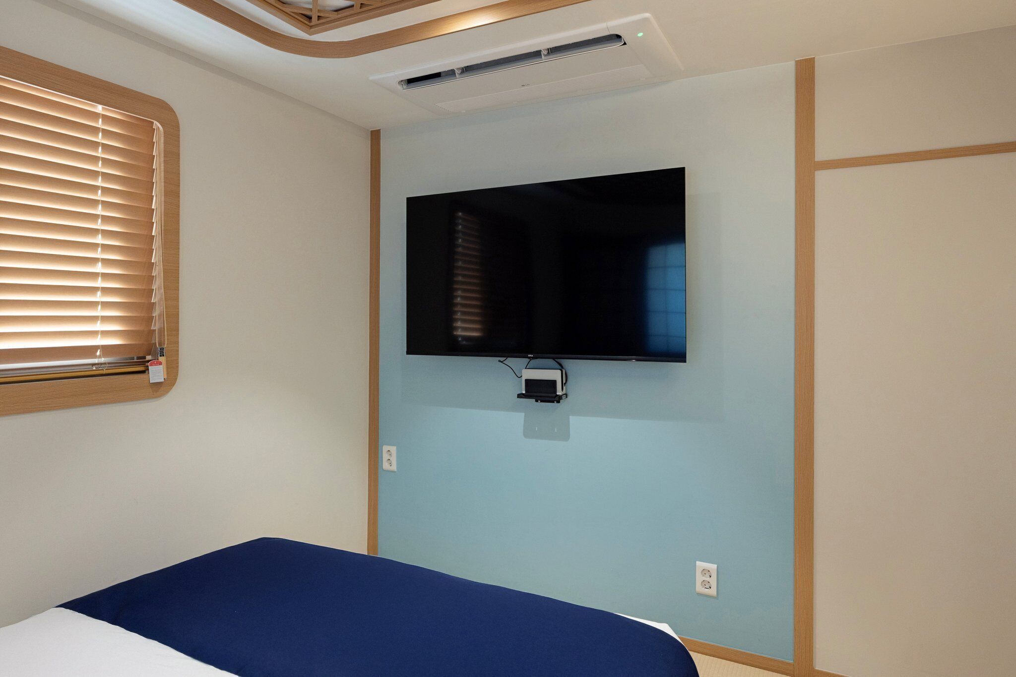 Quarto com cama, televisão montada e janela com persianas.