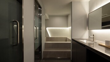 Un baño moderno con cabina de ducha de vidrio, un lavabo con espejo y una escalera que lleva a la zona de la ducha.