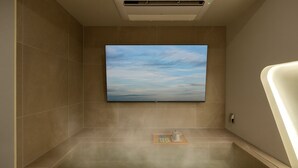 Una sauna con una grande TV a schermo piatto montata a parete, un portascopevoli e un generatore di vapore a pavimento.