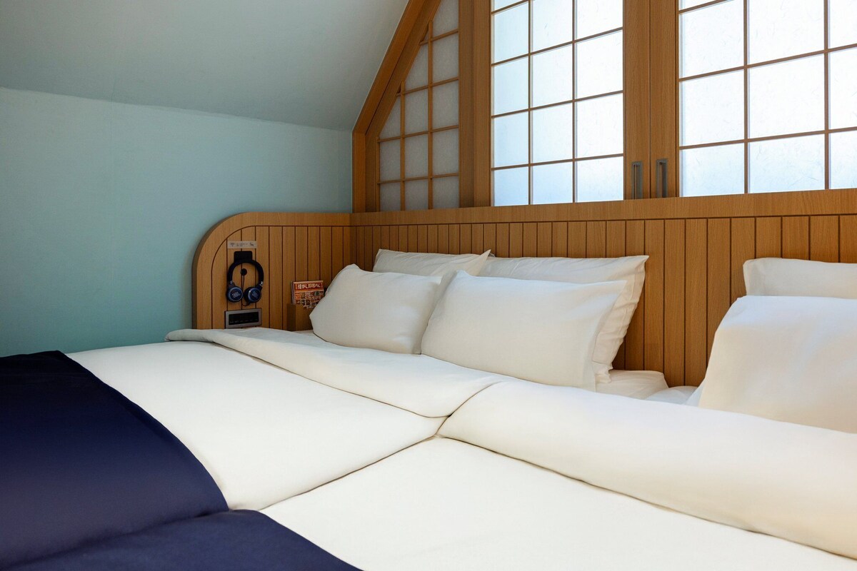 A room with a bed, wooden headboard, and large windows.
