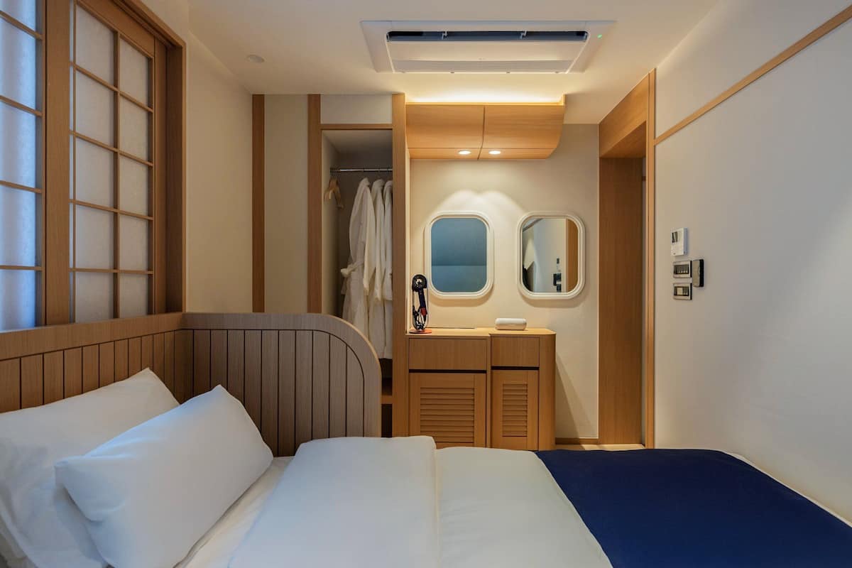 A hotel room with a bed, a vanity with a mirror, a robe, and a window with blinds.