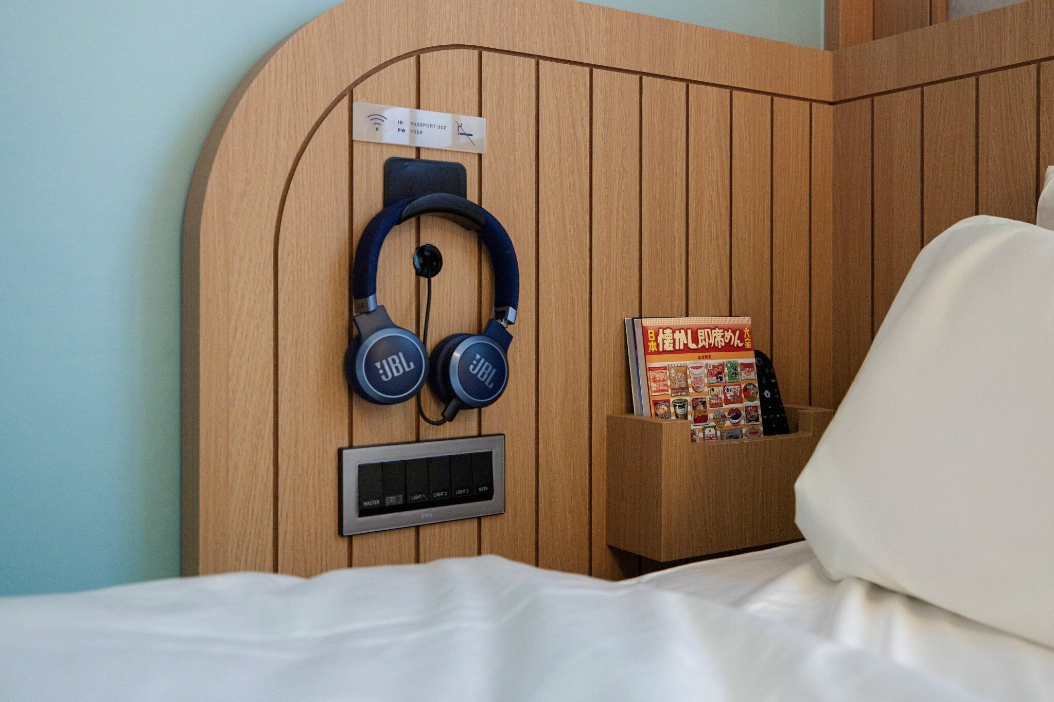A wooden headboard with a pair of JBL headphones, a control panel, and a small shelf with a book.