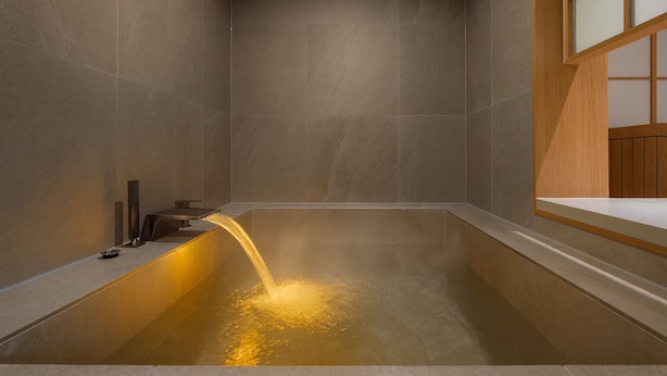 Un bagno moderno con una vasca freestanding, una doccetta a parete e un mobile bagno in legno.