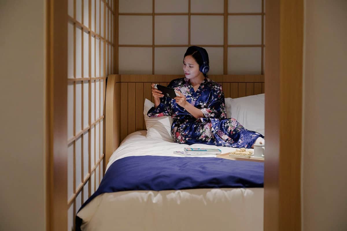 A person sitting on a bed in a room with a wooden headboard and a shoji screen.