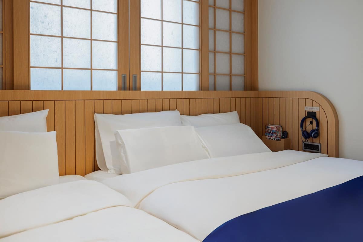 A hotel room with a wooden headboard, a bed with white bedding, and a wall-mounted nightstand with a pair of headphones and a small decorative item.