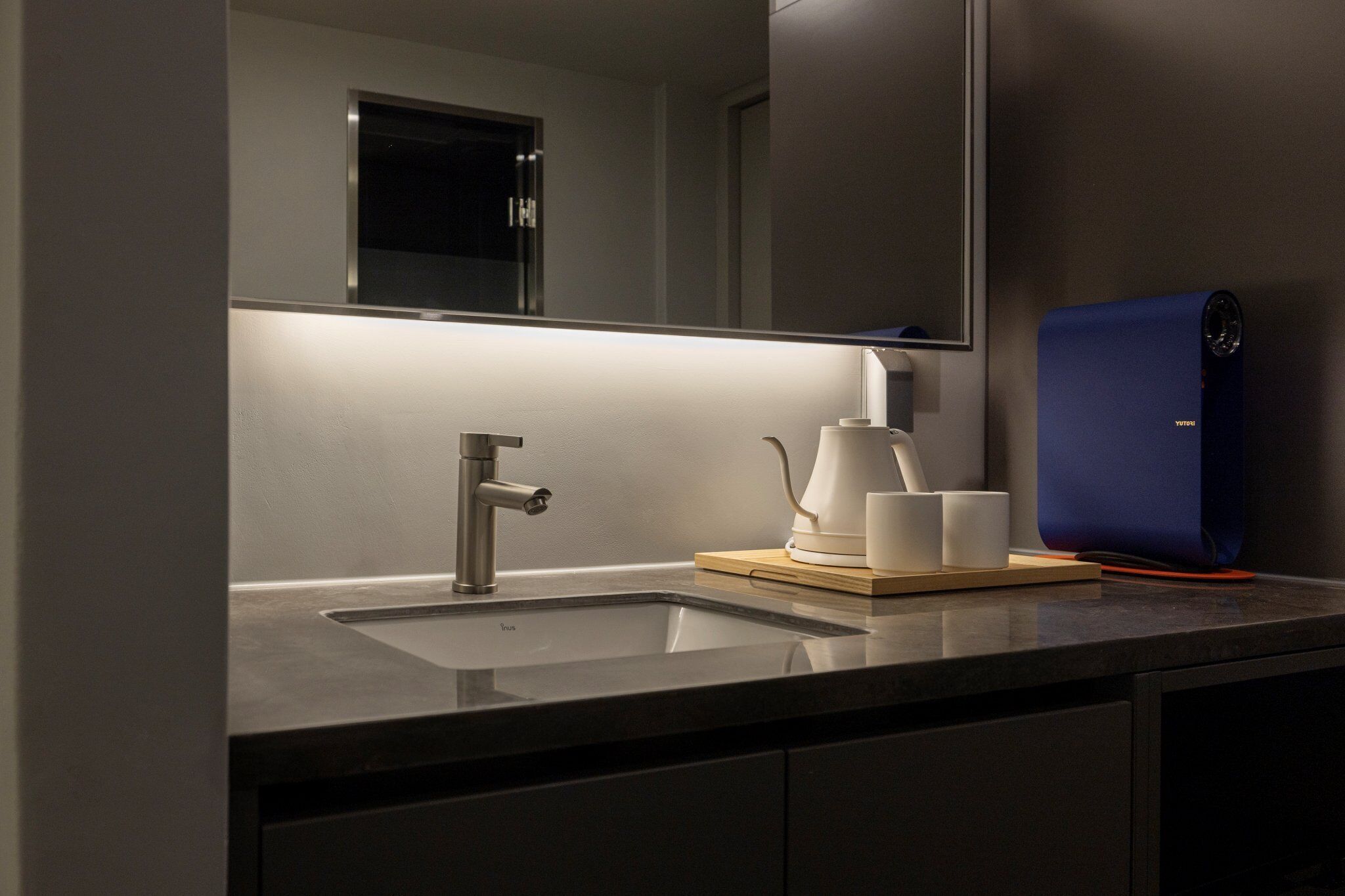 Une salle de bain moderne avec un lavabo, un miroir et un appareil bleu posé sur le comptoir.