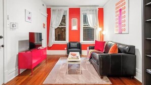 A living room with a red accent wall, a black leather sofa, a red cabinet, and a television. - Chicago Citrus Charm 2BR  WestTown (Chicago)
