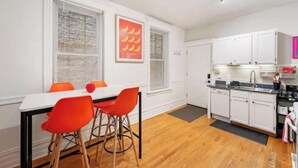 A modern kitchen with white cabinets, a black countertop, and a dining area with a white table and orange chairs. - Chicago Citrus Charm 2BR  WestTown (Chicago)