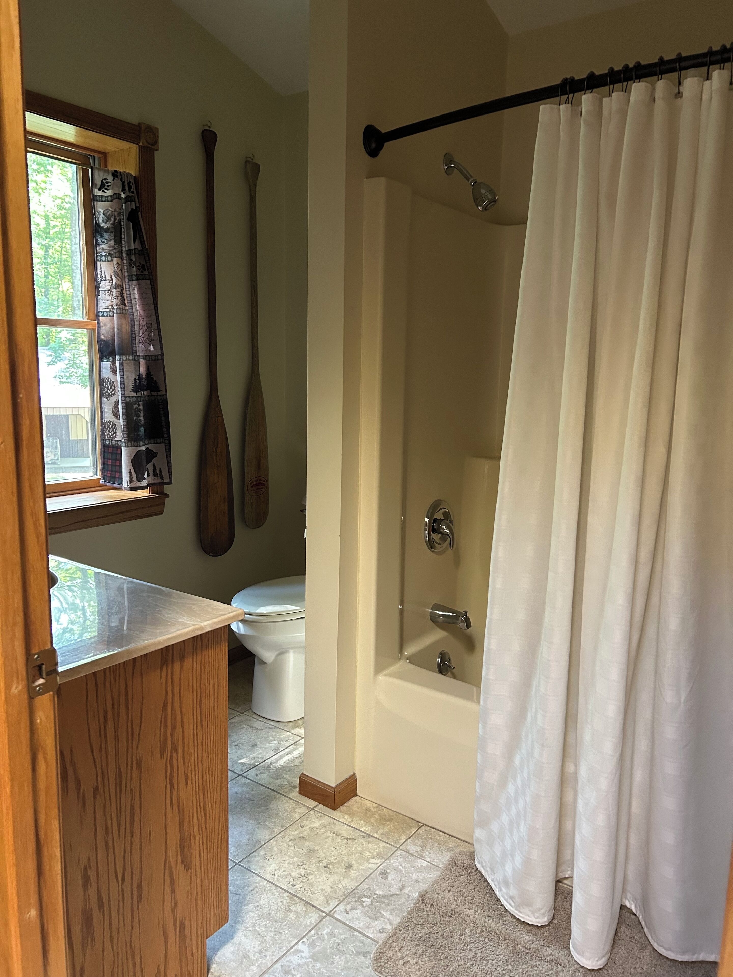 A bathroom with a bathtub, toilet, and a window with curtains.