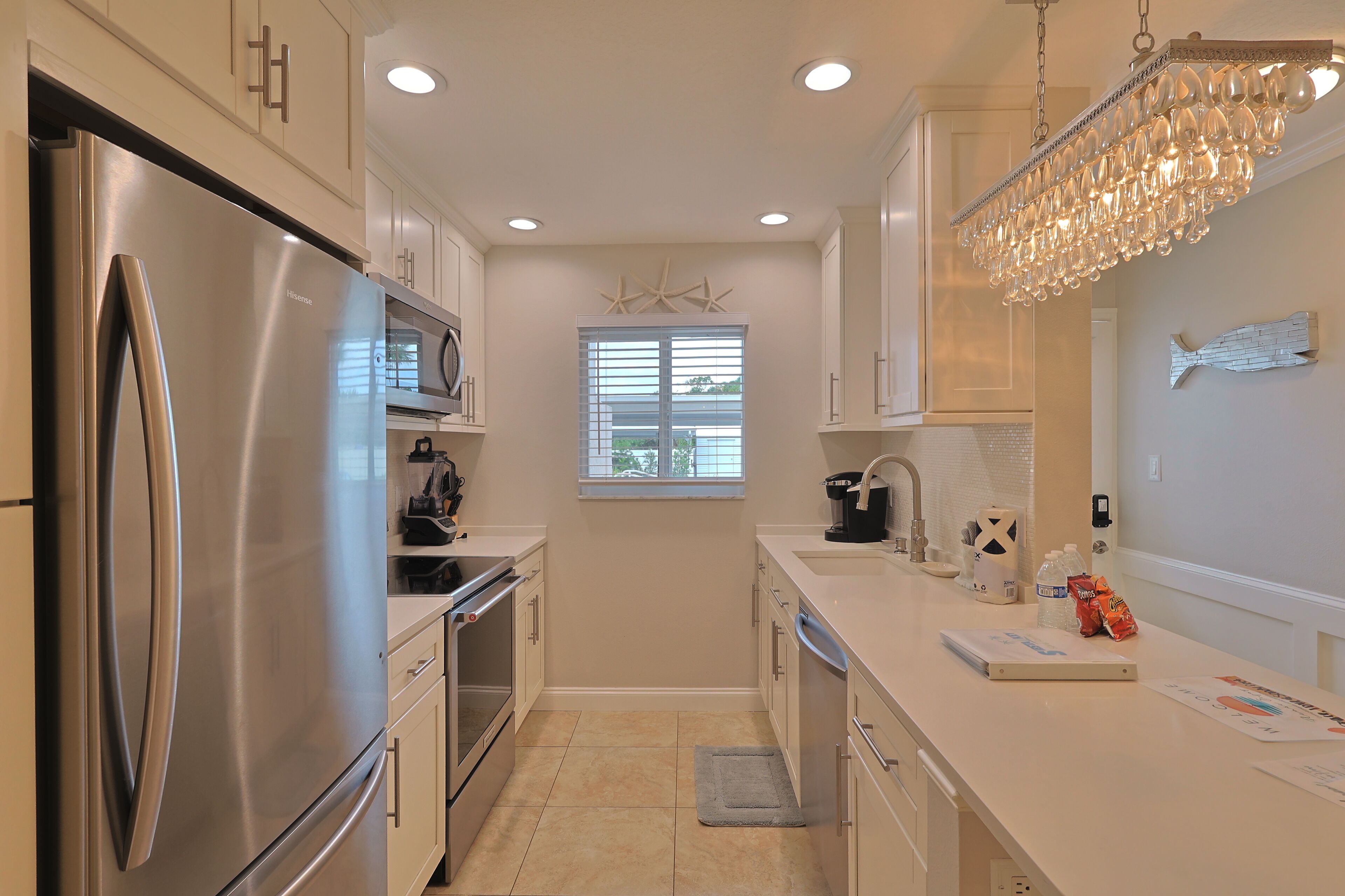 A modern kitchen with stainless steel appliances, a chandelier, and a window with starfish decor.