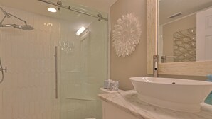 A bathroom with a glass shower enclosure, a white toilet, a marble sink, and a decorative wall piece.