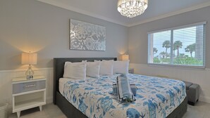 A bedroom with a large bed, a nightstand, a chandelier, a window with blinds, and a decorative wall piece.