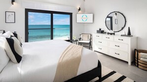 Een slaapkamer met een bed, een kaptafel, een stoel, een ronde spiegel en uitzicht op de oceaan.