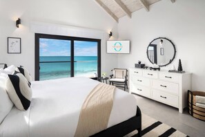 A bedroom with a bed, a dresser, a chair, a round mirror, and a view of the ocean. - Opaline Villa -3BR 2bath Oceanfront (Providenciales)