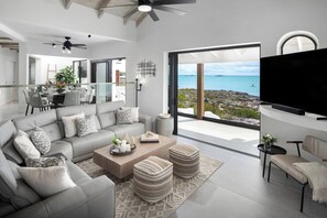 A modern living room with a large TV, grey sofa, and ottomans, with a view of the sea. - Opaline Villa -3BR 2bath Water front (Providenciales)