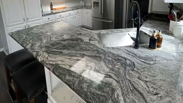 A modern kitchen with white cabinets, a marble countertop, stainless steel appliances, pendant lighting, and a skylight.