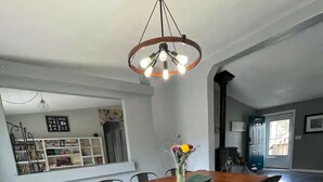 A dining area with a wooden table, metal chairs, a hanging light fixture, and a vase with flowers.