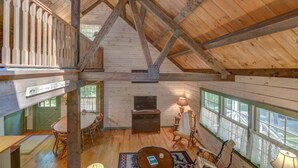 A cabin interior with a loft bedroom, a fireplace, wooden floors, and large windows. - Entire cabin in Speculator, New York (Speculator)