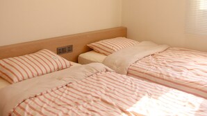 Ein Zimmer mit zwei Betten, jeweils mit gestreifter Bettwäsche, einem hölzernen Kopfteil und einer Wand-Klimaanlage.