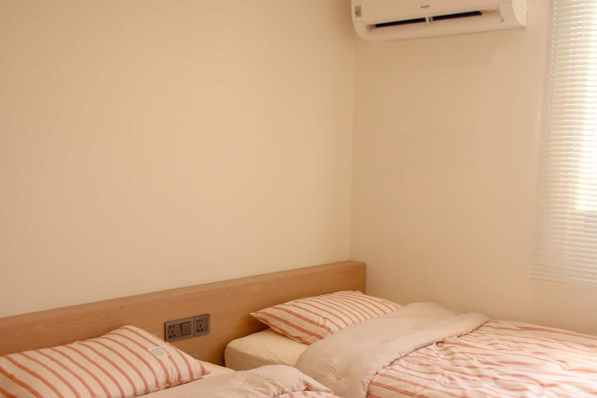 A room with two beds, each with striped bedding, a wooden headboard, and an air conditioning unit mounted on the wall.