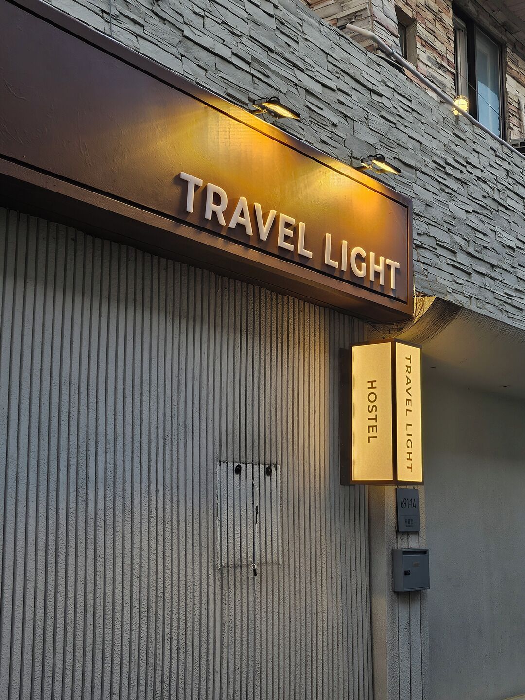 Un edificio con un letrero que dice "TRAVEL LIGHT HOSTEL" y otro letrero separado también con "TRAVEL LIGHT HOSTEL" y el número "69114".
