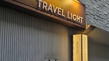 Un edificio con un letrero que dice "TRAVEL LIGHT HOSTEL" y otro letrero separado también con "TRAVEL LIGHT HOSTEL" y el número "69114".
