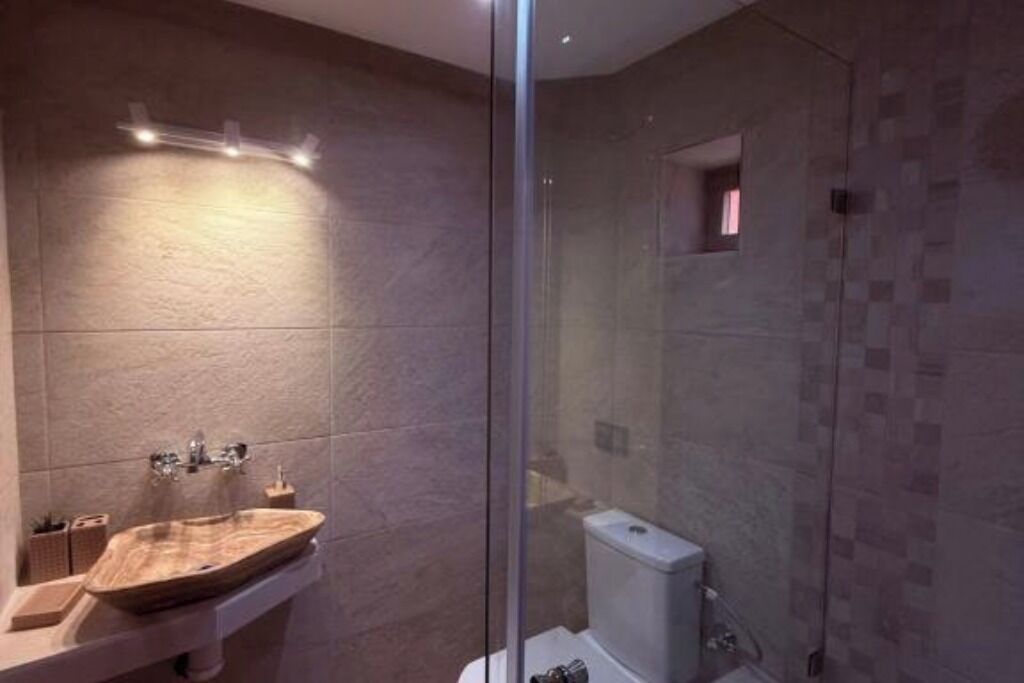 A modern bathroom with a glass shower enclosure, a wooden vanity, and a small window.