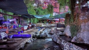 A riverside market with wooden stalls and stone steps alongside a flowing stream. - 3A retreat (Sti Fadma)